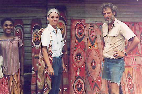 [Wosera girl, Carolyn, Ron, standing in front of bright red bark panels and statues: 52k]